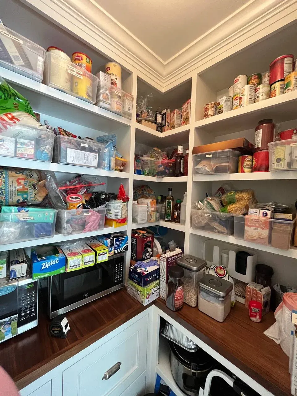 Pantry corner before, packaged goods and snack bags piled on the right wall, with the microwave and counter visible at the bottom of the frame