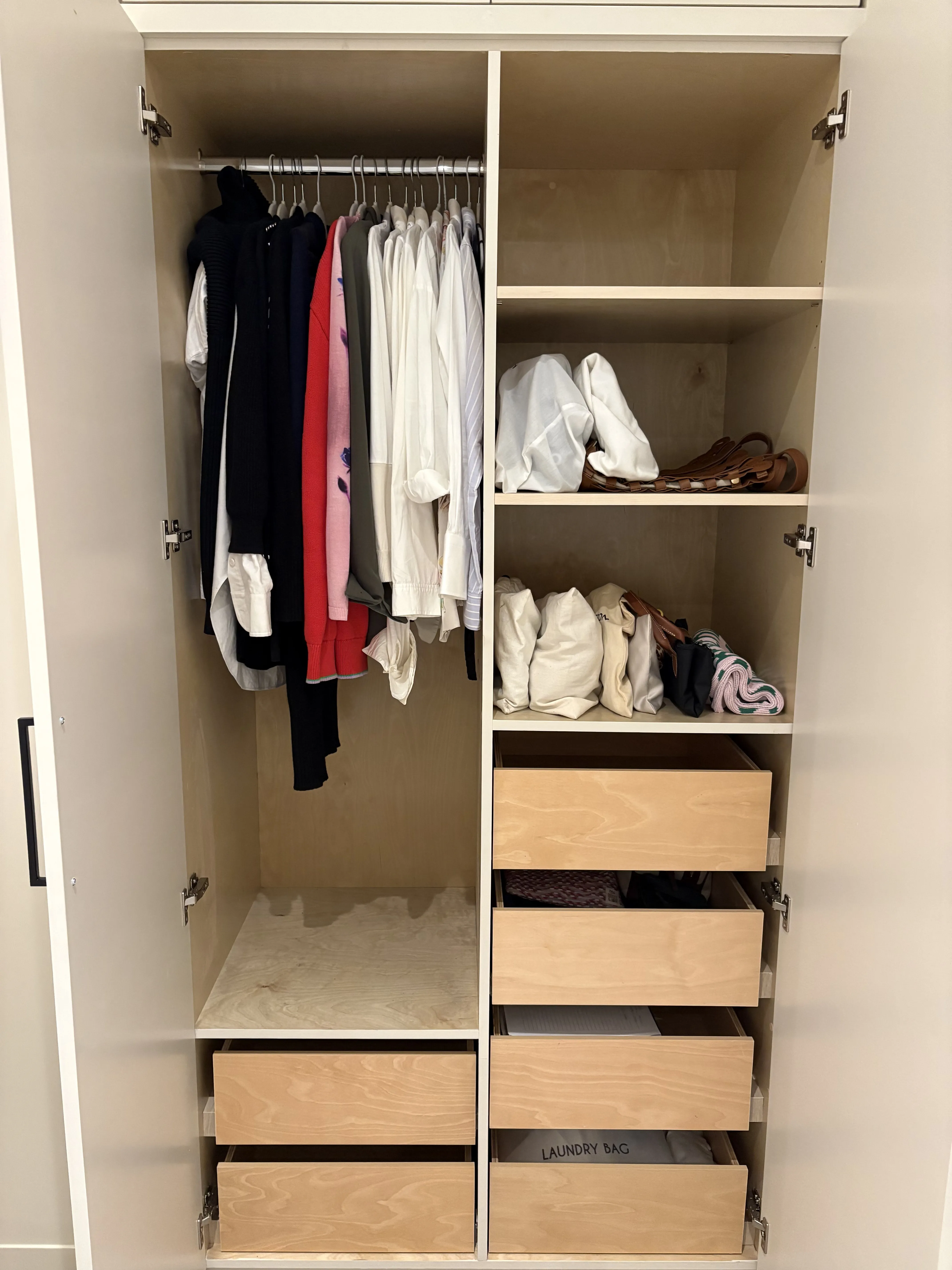Closet with short hung pieces on the left, open shelves of folded white tops and handbags on the right, and a column of drawers below
