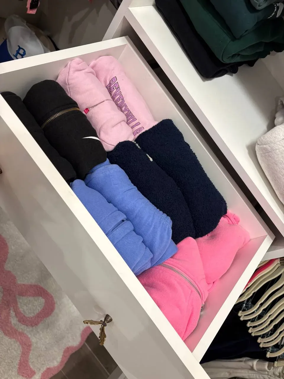 Open drawer of cozy hoodies and sweatshirts rolled and stood on end, sorted by color
