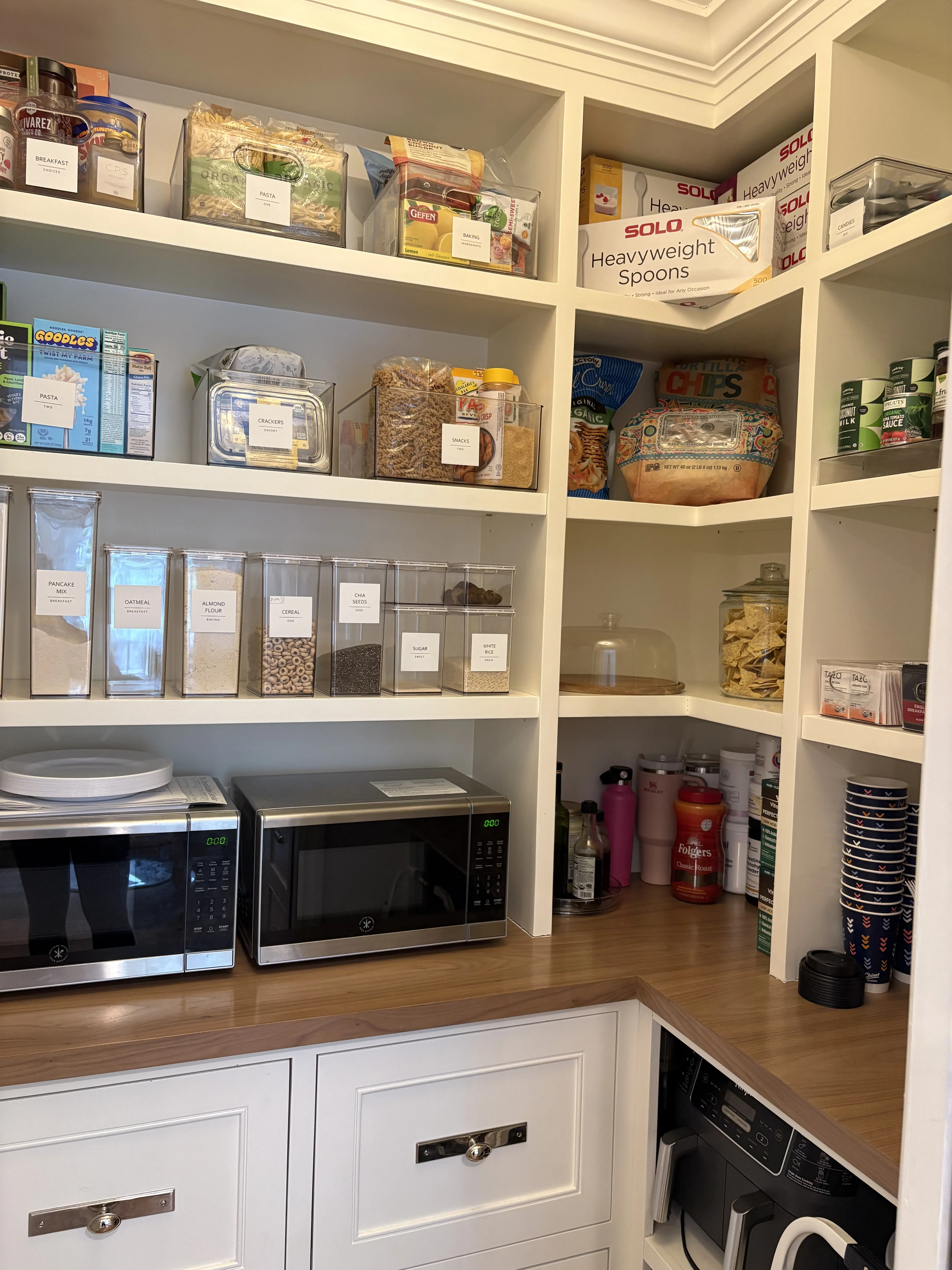 Same pantry wall after, with labeled clear bins, decanted dry-goods containers, and snacks zoned together by category