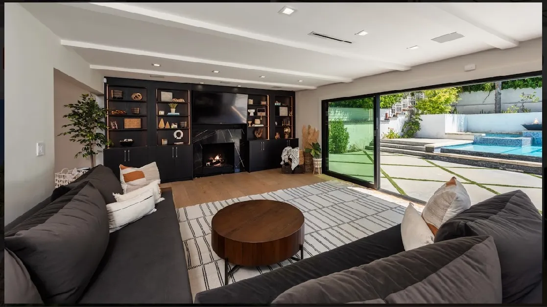 Living area with a low fireplace, built-in media wall, and the pool just beyond the glass