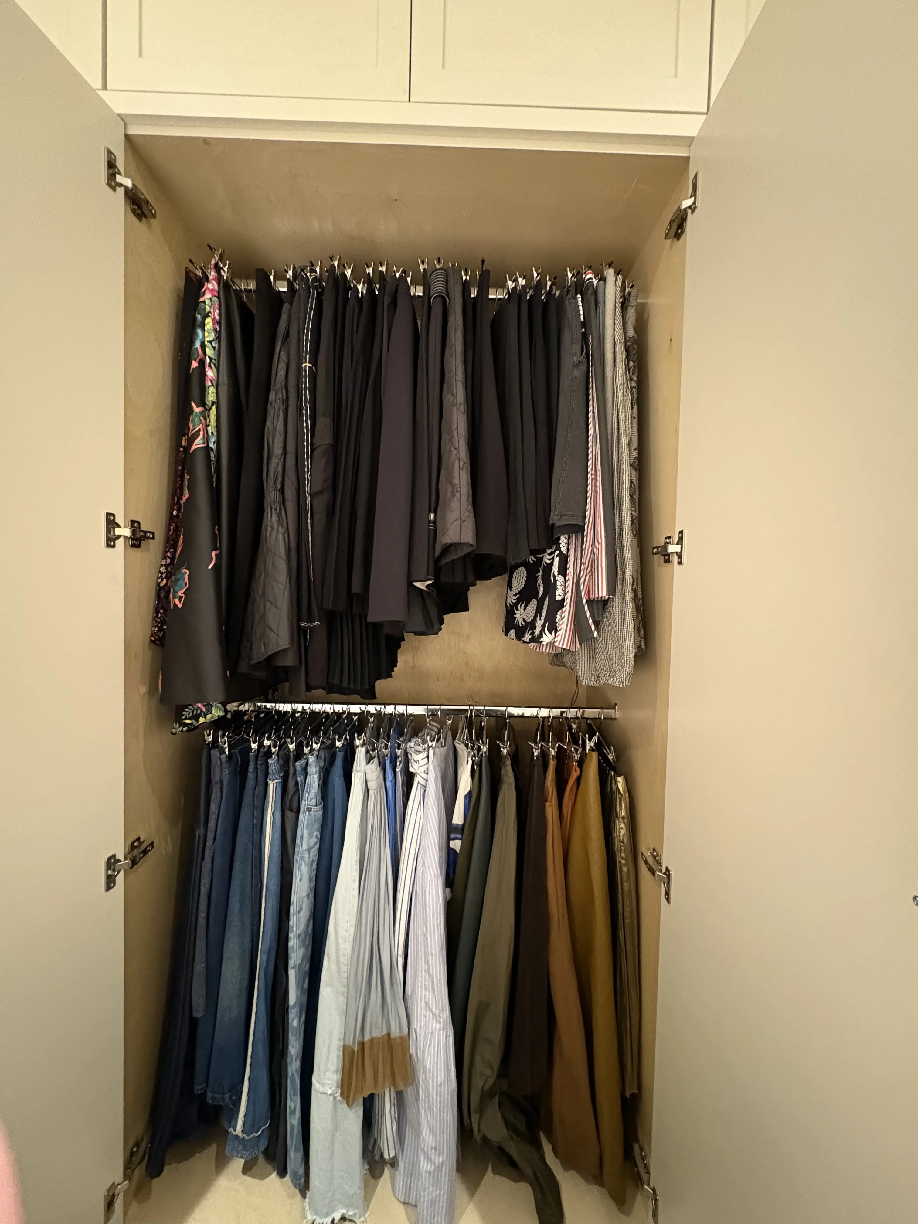 Double-rod closet with dark skirts and dresses on the upper rod and a full row of jeans and pants on clip hangers on the lower rod