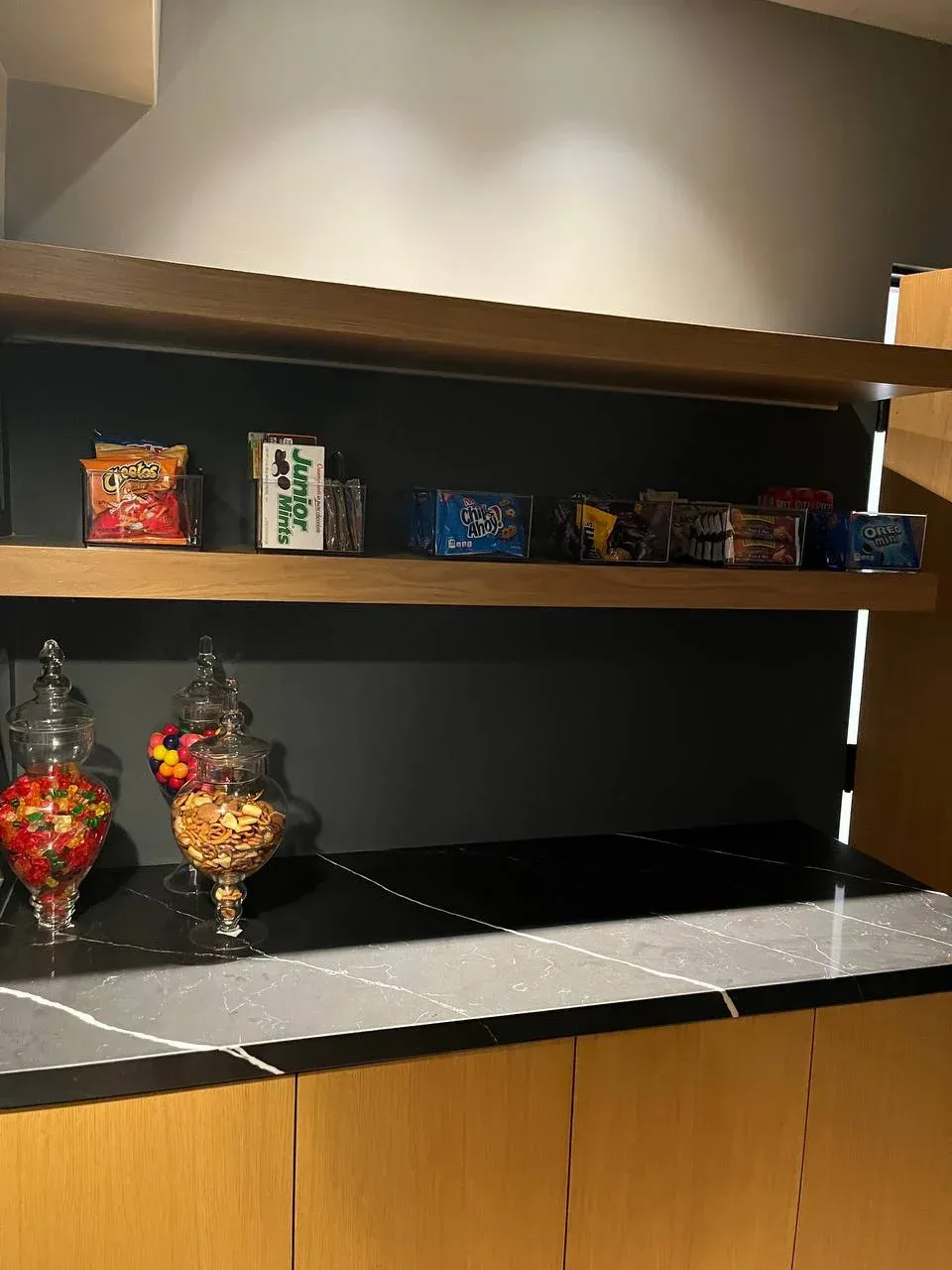 Close view of the snack shelf with clear bins of labeled snacks and apothecary jars of candy and trail mix below