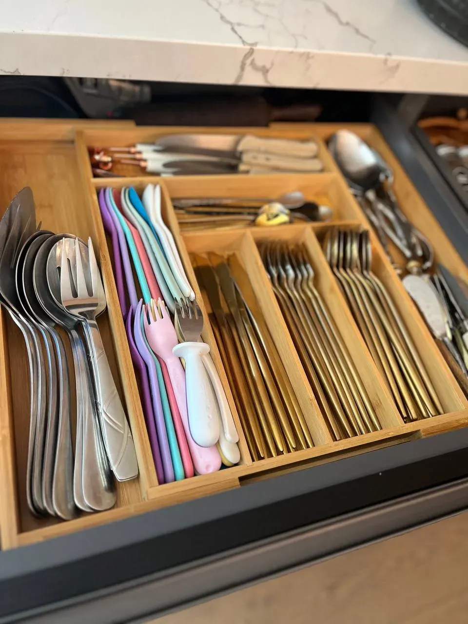 Utensil drawer with adjustable bamboo dividers separating stainless, gold, and kids' flatware by type
