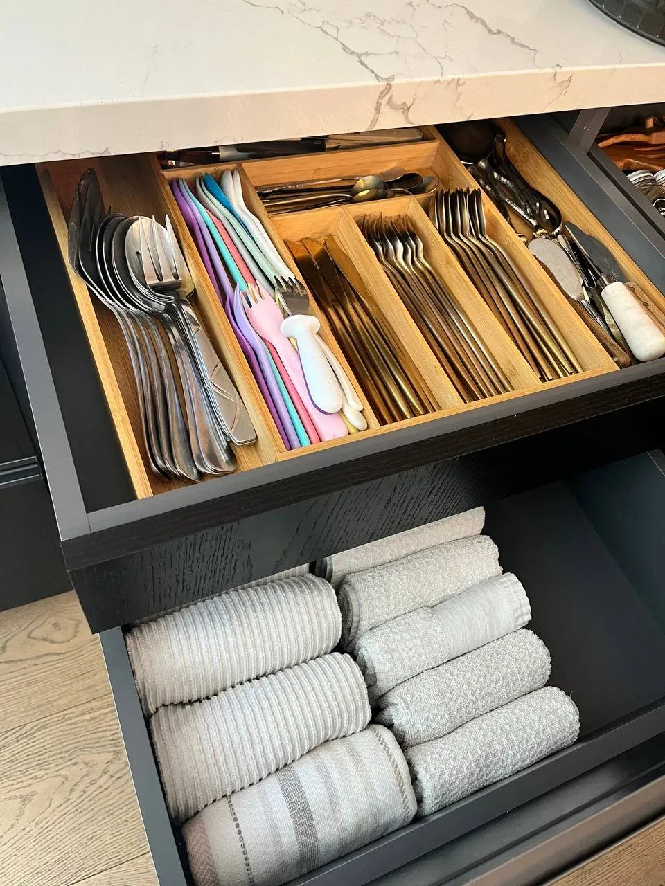 Two open drawers stacked, cutlery in bamboo dividers above and rolled kitchen towels below