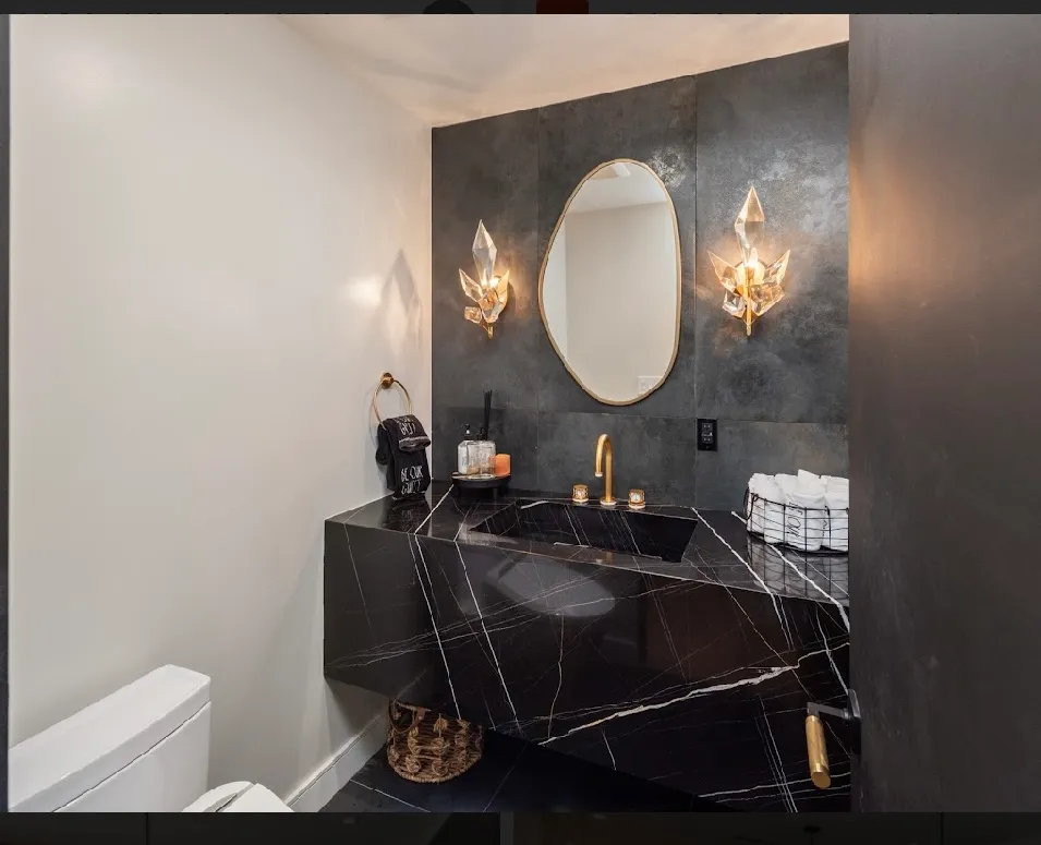 Powder room finished in dark veined marble with sconces flanking an oval mirror