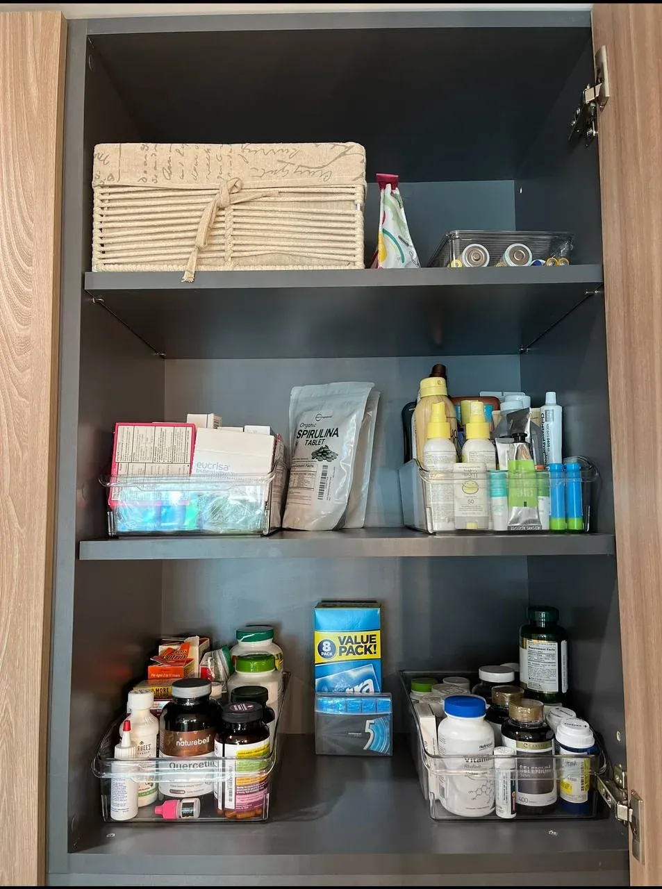 Cabinet of vitamins, medicines, and sunscreens sorted into clear bins across three shelves