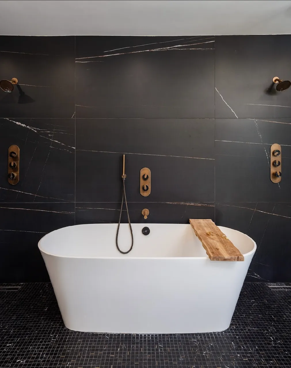 Freestanding tub against a dark marble feature wall with brass fixtures