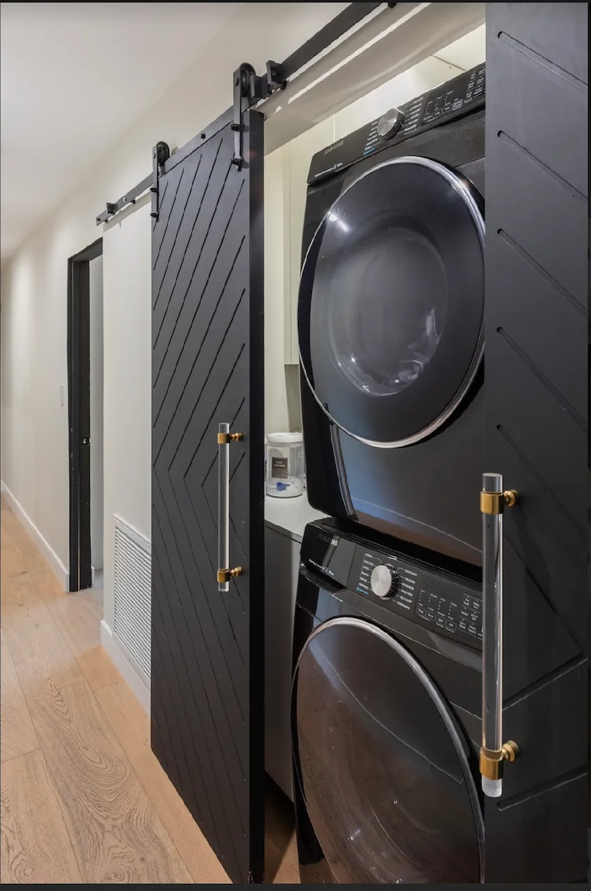 Laundry with stacked black washer and dryer behind sliding barn doors