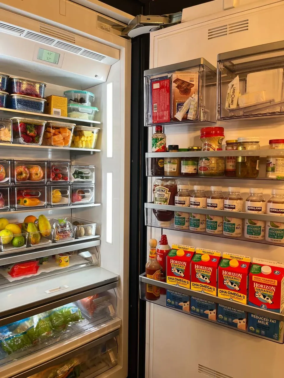 An open refrigerator fully stocked, with clear pull-out bins, produce drawers sorted by color, and the door grouped by type