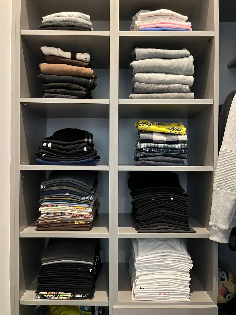 Close-up of grey cubby shelves with sweatshirts and tees folded into neat, color-sorted stacks