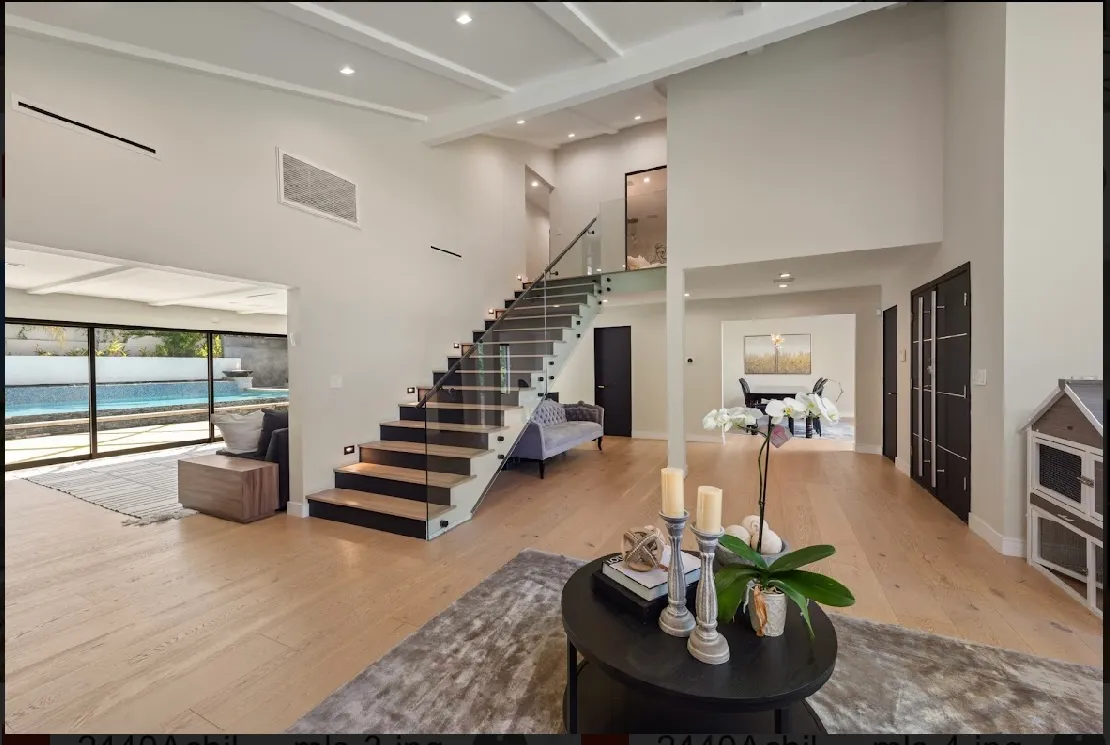 Open-concept great room with vaulted ceilings, an open-tread staircase, and floor-to-ceiling sliders out to the pool