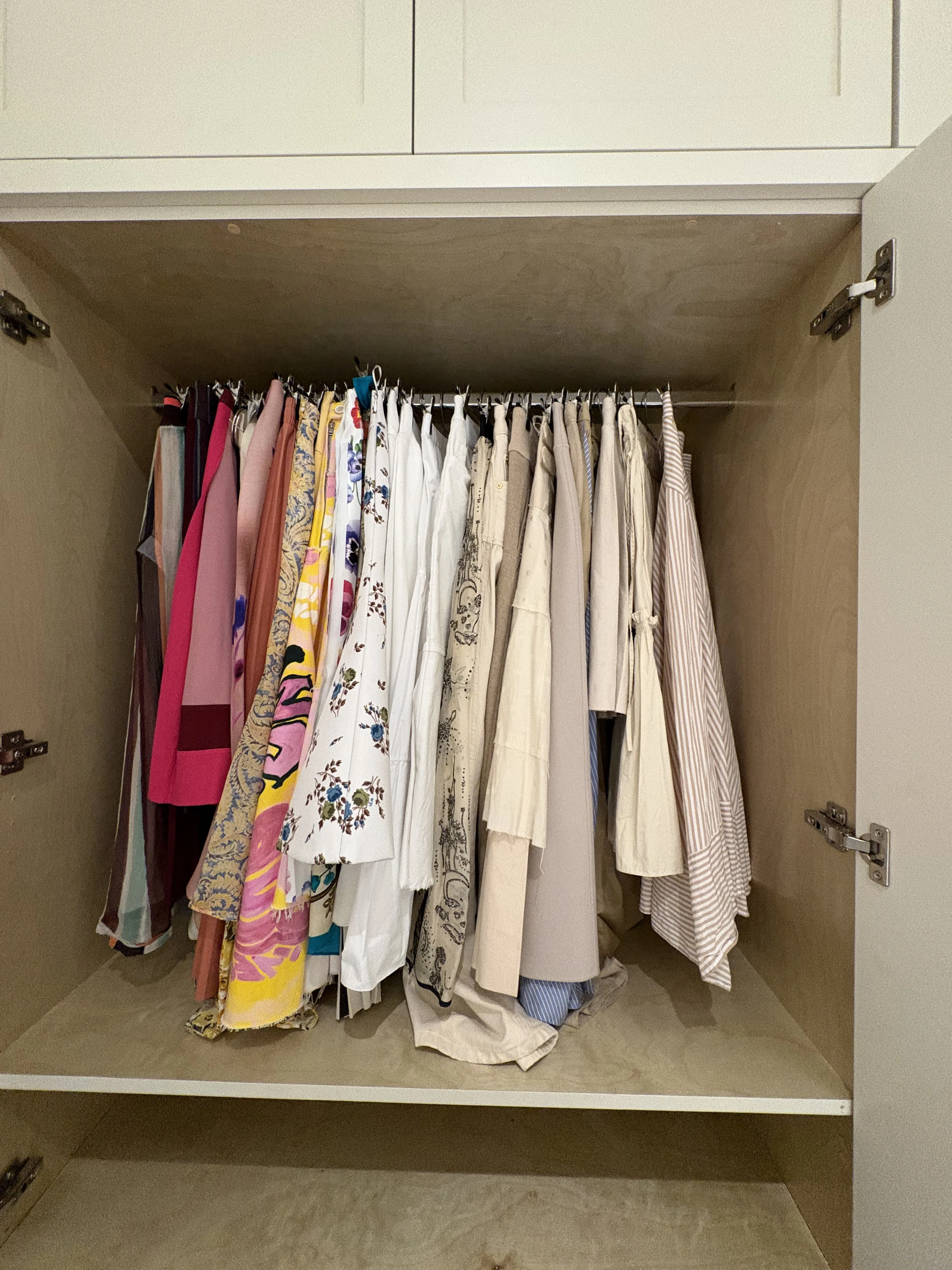Open closet rod hung with long dresses and skirts in pinks, whites, and patterned silks, with light tops and white cottons across the right side