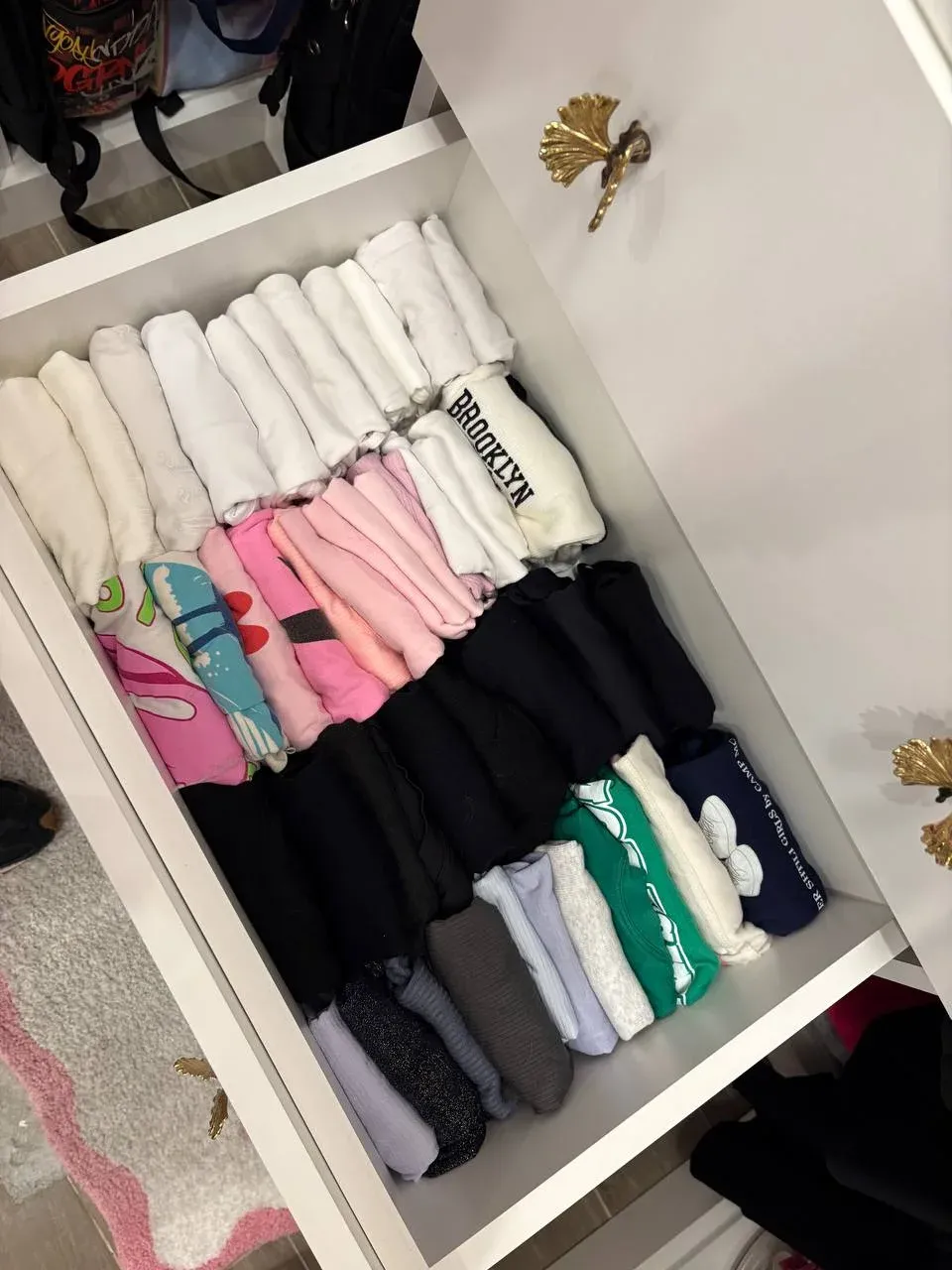 Open drawer of tops rolled and stood on end, sorted from white through pink to black and green