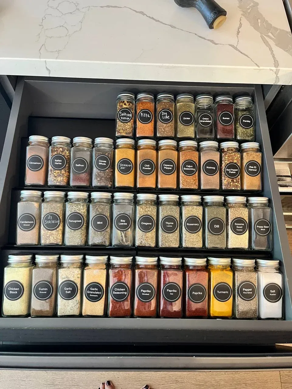 Spice drawer with rows of identical labeled jars set into a tiered insert that lifts the back rows higher than the front